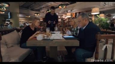一家人在餐厅吃饭，女人在吃饭，而年长的男人在用平板电脑工作